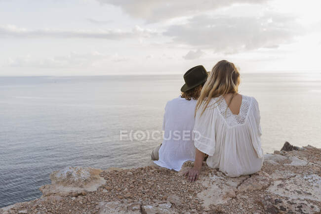 Visão traseira do jovem casal sentado na rocha em frente ao mar, Ibiza, Ilhas Baleares, Espanha — Fotografia de Stock