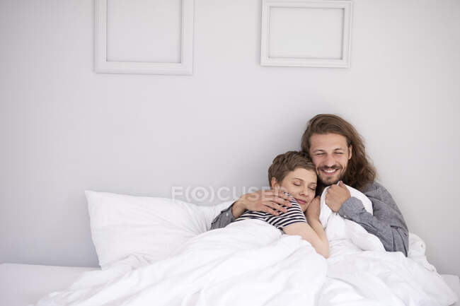 Feliz joven pareja abrazándose en la cama en casa - foto de stock