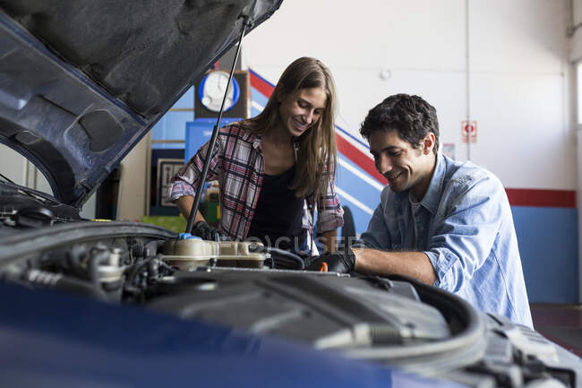 Cheerful man and young woman working together on car repair service and fixing car engine — Stock Photo