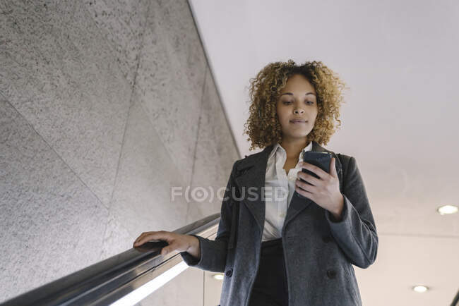 Mujer usando teléfono celular en escaleras mecánicas - foto de stock