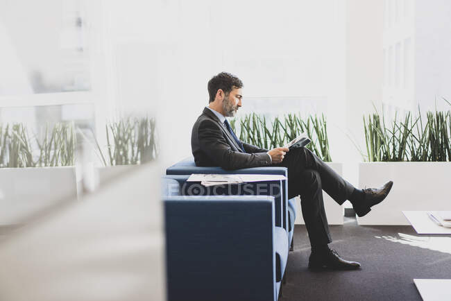 Зрілий бізнесмен сидить у залі очікування, читаючи журнал — стокове фото
