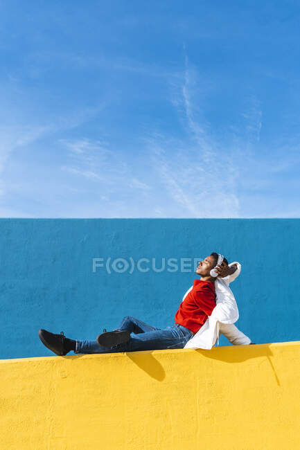 Young dancer sitting on yellow wall, listening music — Stock Photo