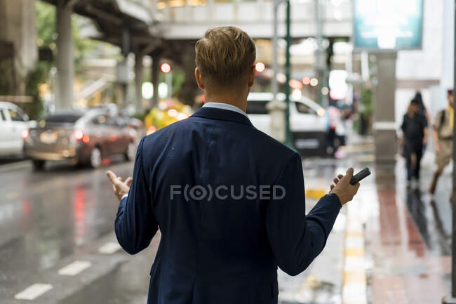 Young businessman holding smartphone in Bangkok during a rainy day — Stock Photo
