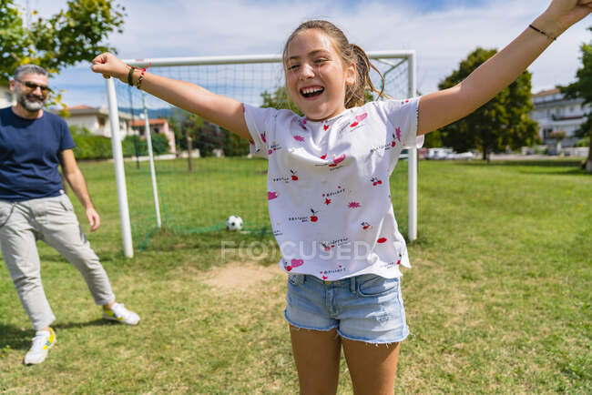 Счастливая девушка играет в футбол с отцом на лугу — стоковое фото