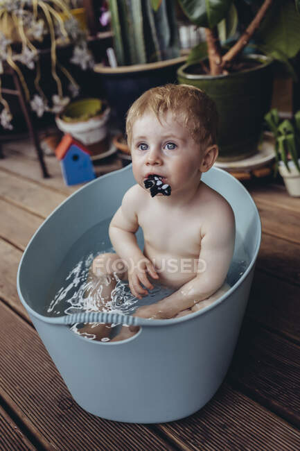 Petit garçon assis dans le bain de bébé sur le balcon, jouant avec un jouet — Photo de stock