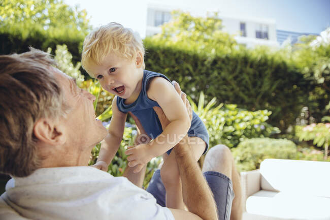 Отец сидит в саду, играет со своим маленьким сыном — стоковое фото