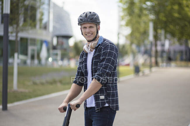 Портрет усміхненого молодого чоловіка з електронним скутером у місті. — стокове фото