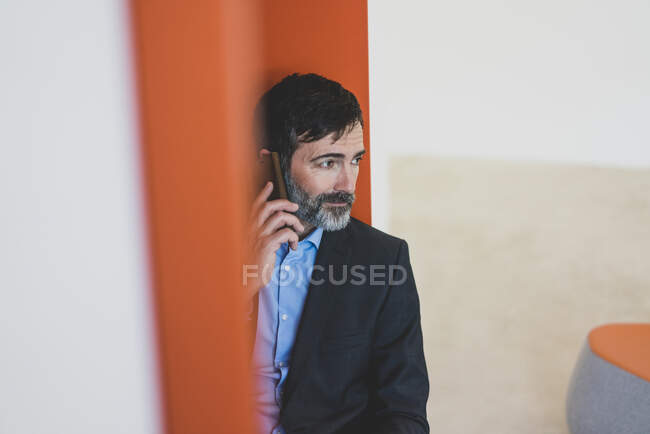 Зрелый бизнесмен, сидящий в нише и разговаривающий по мобильному телефону — стоковое фото