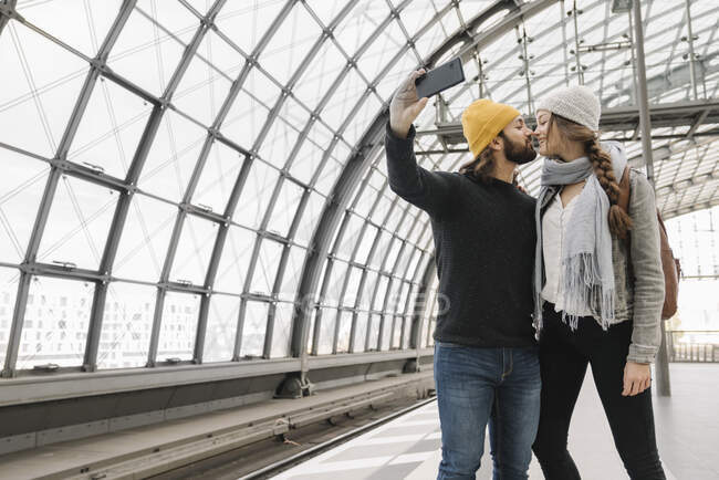 Young couple kissing and taking a selfie at the station platform, Berlin, Germany — Stock Photo