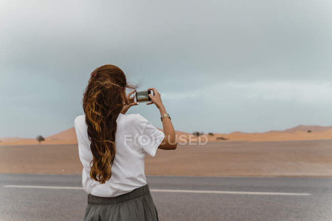 Back view of young woman standing  roadside taking photo with smartphone, Fez, Morocco — Stock Photo