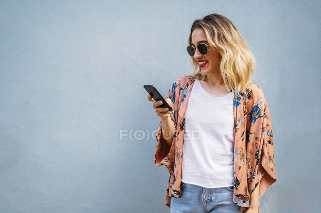 Femme blonde souriante utilisant un smartphone, fond bleu — Photo de stock