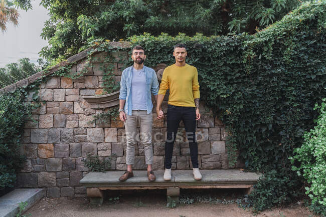 Портрет гей-пары, стоящей рука об руку на каменной скамейке — стоковое фото
