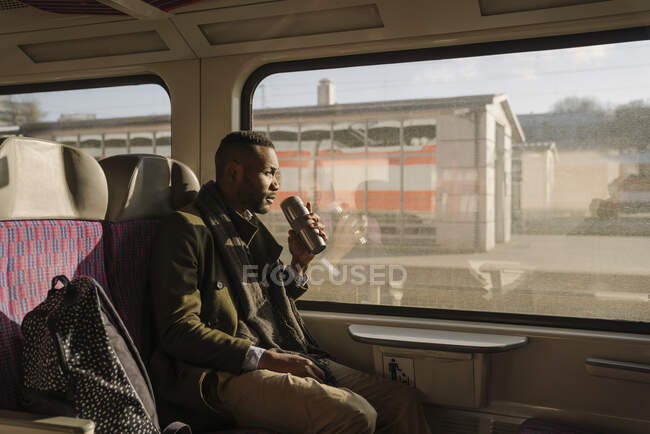 Stylish man drinking hot drink from reusable cup while traveling by train — Stock Photo