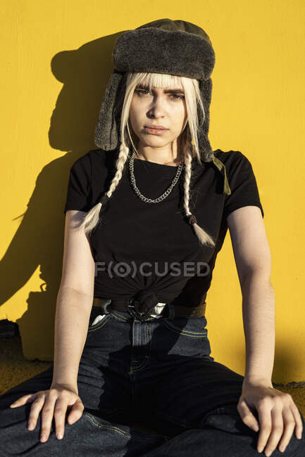 Портрет молодої жінки з блондинками в шапці, що сидить перед жовтою стіною — стокове фото