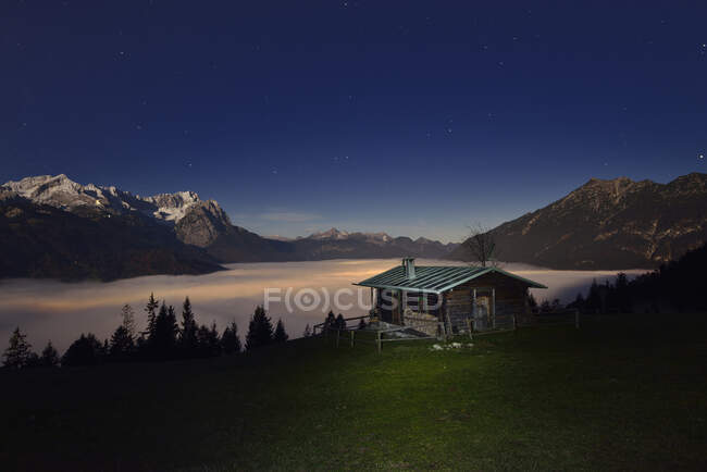 Baita di legno a Mt. Masturbarsi con il bellissimo Monte Zugspitze e il paesaggio nuvoloso di notte, Baviera, Germania — Foto stock