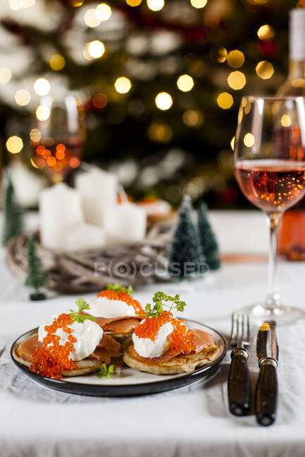 Blinis com creme azedo, salmão defumado e ovas de peixe, na frente da decoração de Natal — Fotografia de Stock