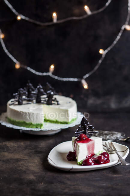Pezzo di cheesecake senza cottura, decorato con alberi di Natale al cioccolato sul piatto con salsa di ciliegie piccanti — Foto stock