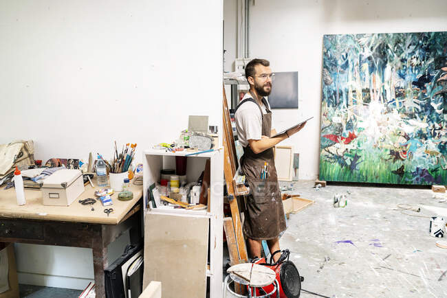 Художник стоїть у своїй студії, тримаючи цифровий планшет — стокове фото