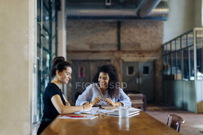 Zwei junge Geschäftsfrauen unterhalten sich am Konferenztisch im Loft-Büro — Stockfoto