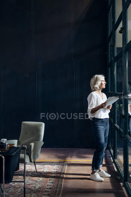 Casual donna d'affari matura guardando fuori dalla finestra in ufficio loft — Foto stock