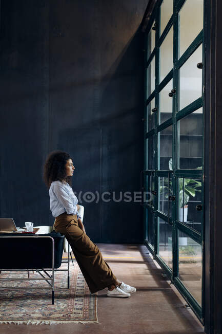 Молода бізнес-леді, дивлячись з вікна в офісі лофт — стокове фото