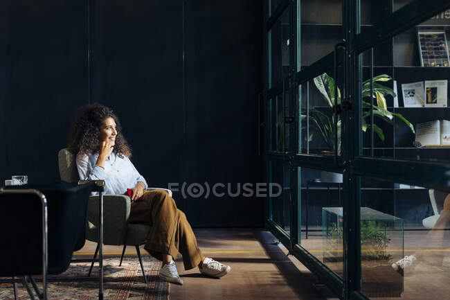 Casual young businesswoman looking out of window in loft office — curly,  self employment - Stock Photo | #466529414