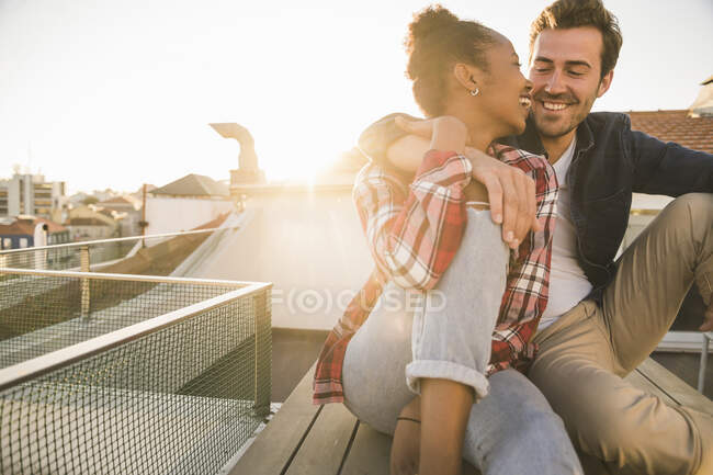 Heureux jeune couple affectueux assis sur le toit au coucher du soleil — Photo de stock