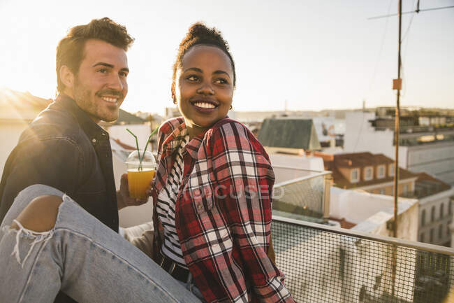 Feliz jovem casal tomando uma bebida no telhado à noite — Fotografia de Stock