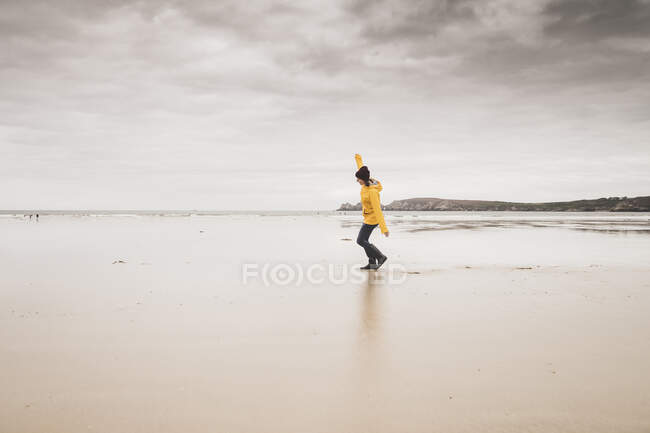 Jeune femme vêtue d'une veste de pluie jaune à la plage, Bretagne, France — Photo de stock