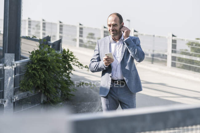 Уверенный зрелый бизнесмен с наушниками и смартфоном на парковке — стоковое фото