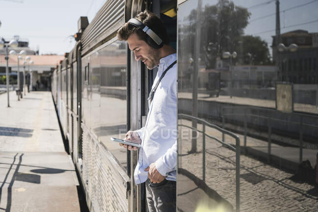 Young man with headphones and smartphone standing in train door — Stock Photo