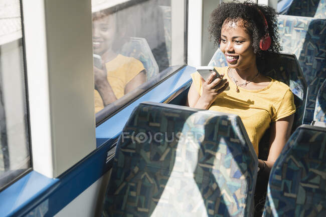Giovane donna sorridente con cuffie e smartphone su un treno — Foto stock