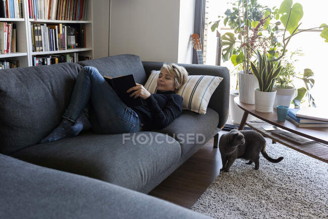 Зрелая женщина отдыхает дома на диване и читает книгу. — стоковое фото