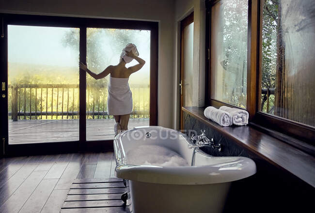 Femme enveloppée dans une serviette regardant par la fenêtre — Photo de stock