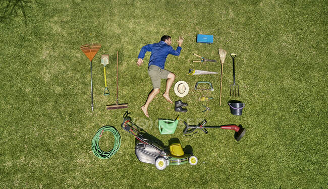 Blick von oben auf einen Gärtner im Liegen auf dem Rasen mit allen Werkzeugen, die er für die Pflege des Gartens braucht — Stockfoto