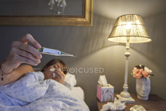 Sick woman laying in the bed and checking her temperature on the thermometer — Stock Photo