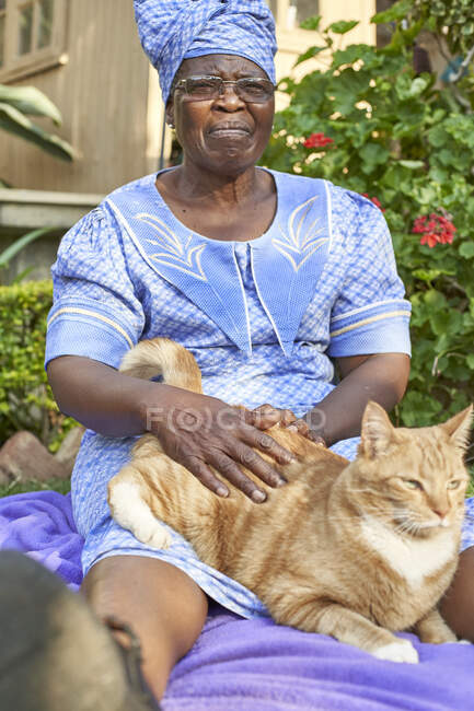 Старшая женщина с котом, сидящей на одеяле в саду — стоковое фото