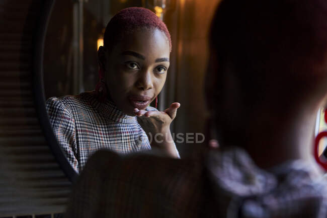 Young woman with short haircut looking to her reflection and sending a kiss in a mirror — Stock Photo