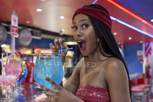 Молодая женщина с плетеной прической сидит в баре ресторана и пьет синий коктейль — стоковое фото