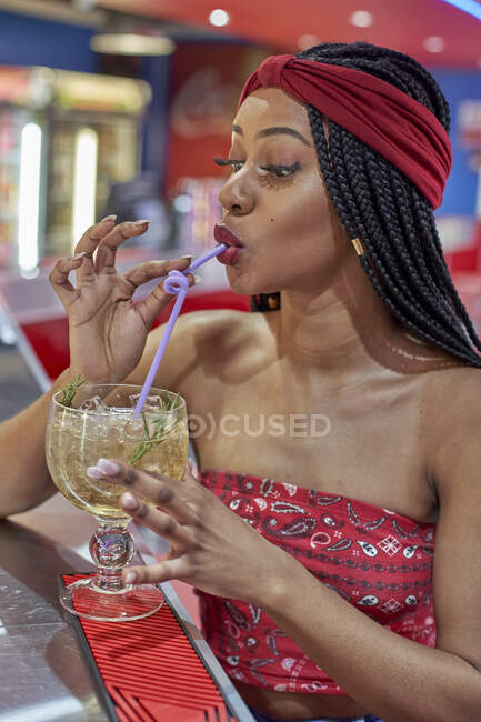 Молодая женщина с плетеной прической сидит в баре ресторана и пьет коктейль с соломинкой — стоковое фото