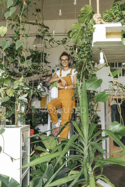 Portrait of a young woman standing on a ladder in a small gardening shop — Stock Photo