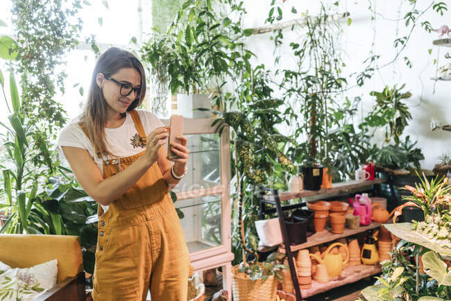 Молодая женщина фотографирует смартфон в маленьком садовом магазине — стоковое фото