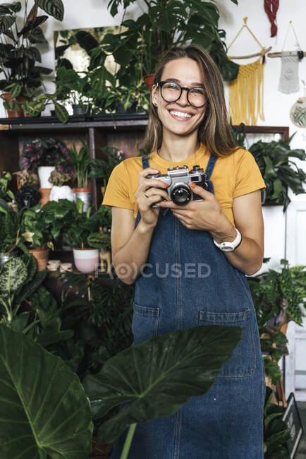 Портрет счастливой молодой женщины с камерой в маленьком садовом магазине — стоковое фото