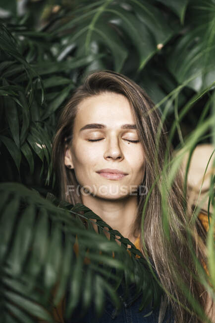 Retrato de una joven con los ojos cerrados en medio de plantas verdes - foto de stock