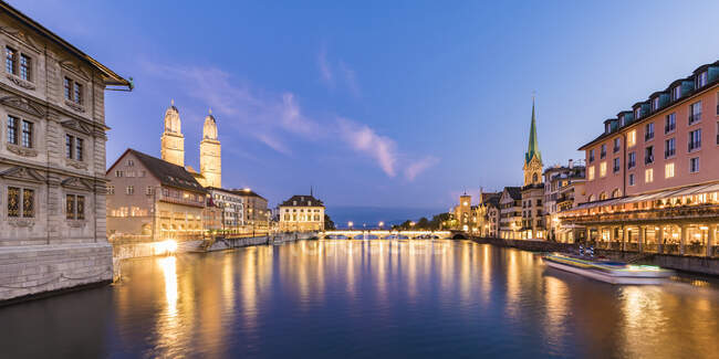 Switzerland, Canton of Zurich, Zurich, River Limmat between illuminated old town waterfront buildings at dusk — Stock Photo