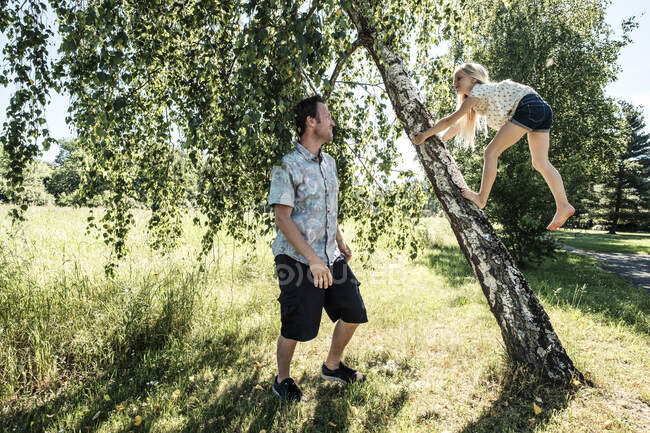 Pai assistindo filha escalando um tronco de bétula no parque — Fotografia de Stock