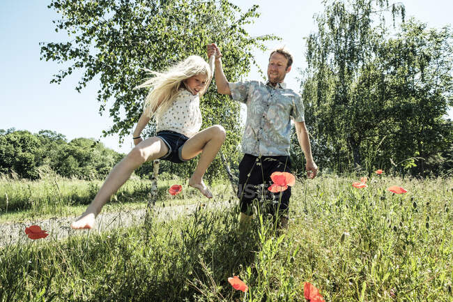 Padre con hija saltando en el prado de amapola - foto de stock
