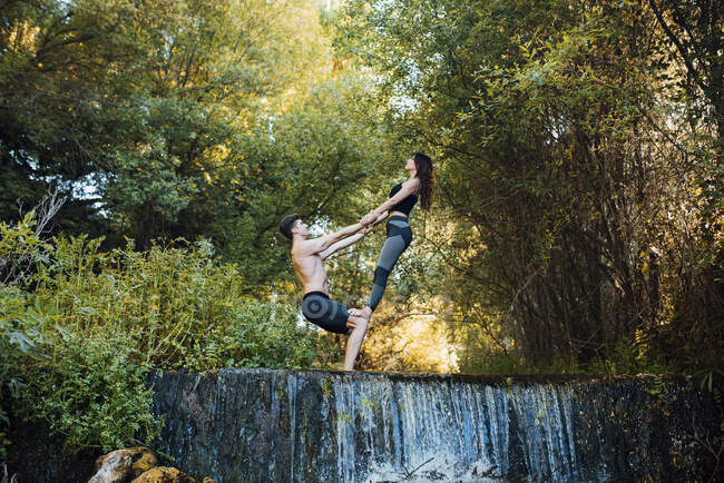 Пара практикующих акро-йогу вместе на водопаде — стоковое фото