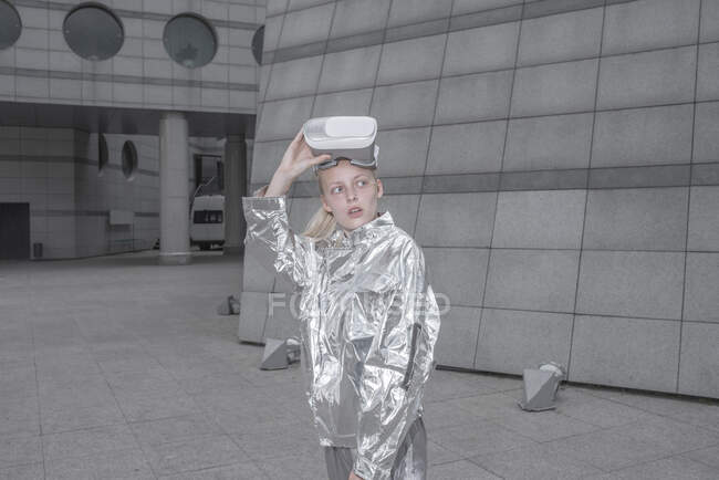 Menina legal em terno de prata vestindo óculos VR em uma cidade futurista — Fotografia de Stock
