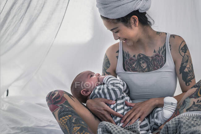 Happy tattooed young woman with her baby in canopy bed — Stock Photo